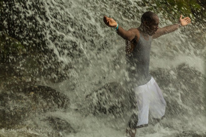 A man spreads his arms under the falls of Saut d'Eau.