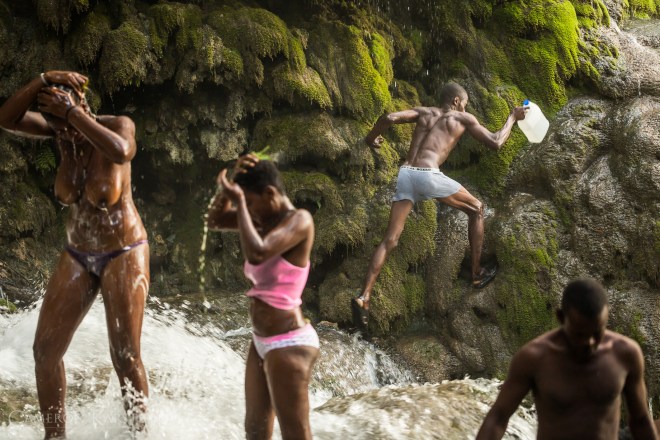 A man climbs the slick rocks to retrieve water from the waterfall to bring with him on his return home.